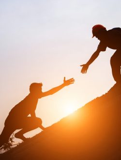 Tourists go up the hill in the sunrise to shake hands The male traveler shakes the hand of the male traveler who is climbing to the top of the hill